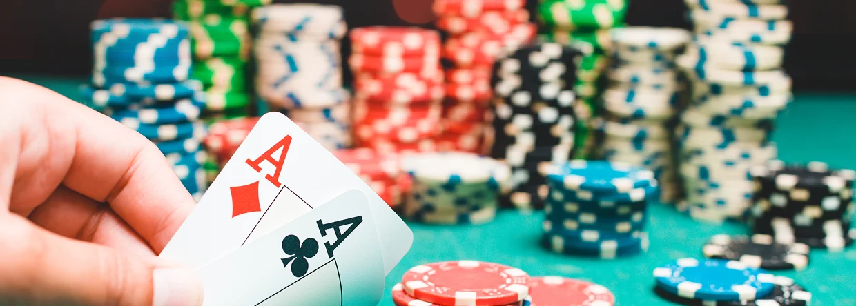 Een hand houdt twee azen vast op een groene pokertafel, met stapels kleurrijke pokerchips op de achtergrond, wat een casino-sfeer met hoge inzetten uitstraalt